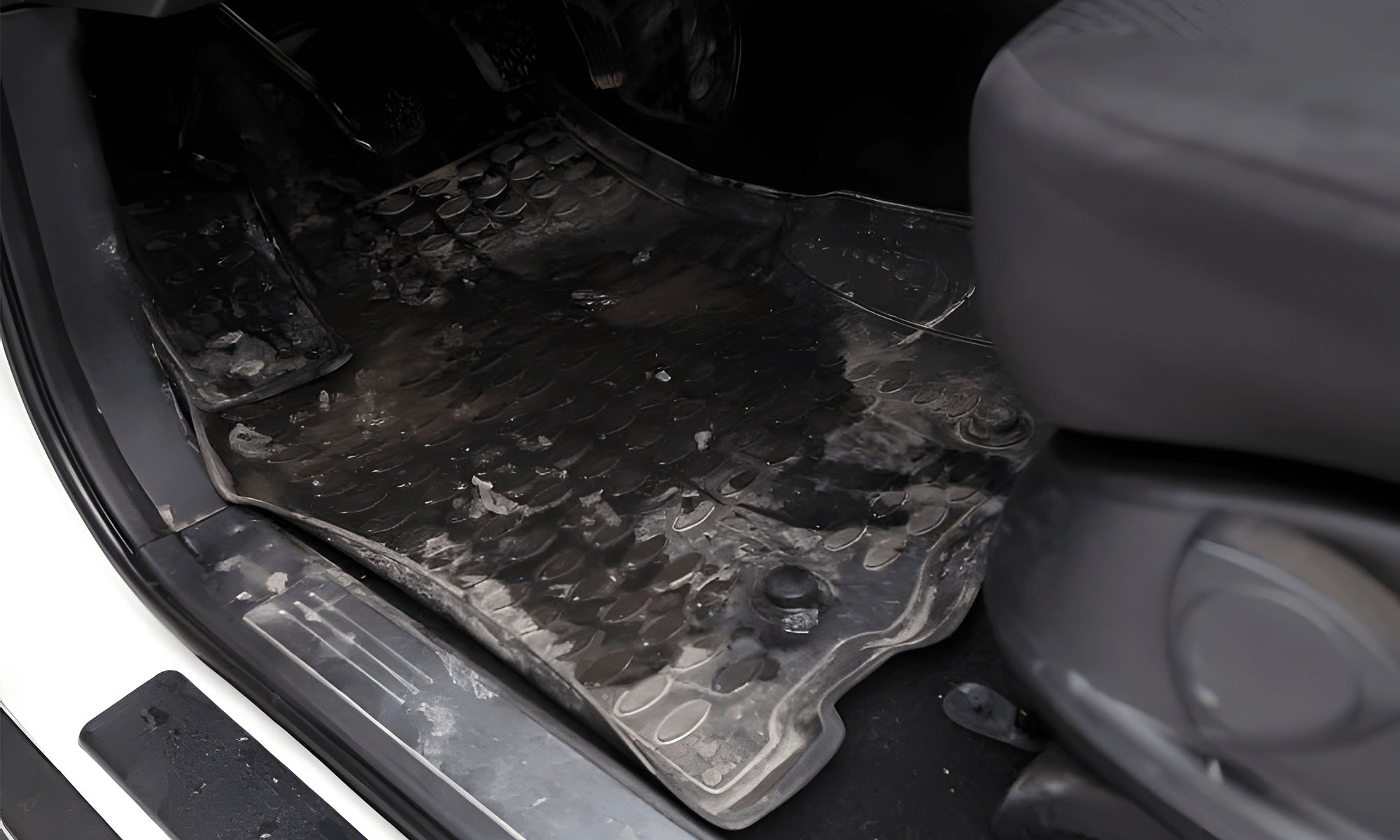 Dirty muddy black rubber car floor mat on driver side showing waterproof protection against mud and debris.