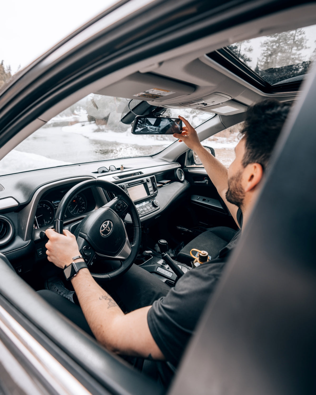 A driver adjusting a rearview mirror dash cam inside a Toyota vehicle.